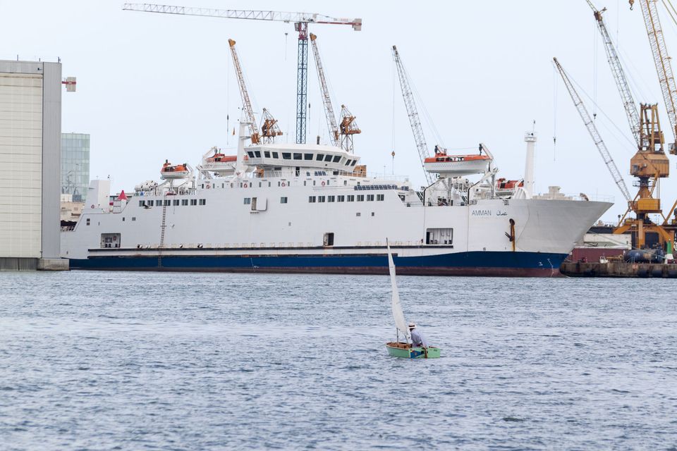 Small sailing dinghy in front of a white ship and port cranes
