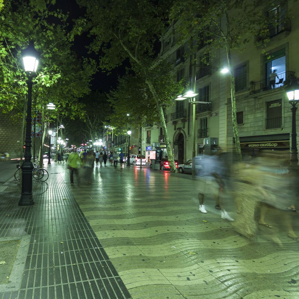 Tree-lined Rambla at night with blurred walkers and wavy paving
