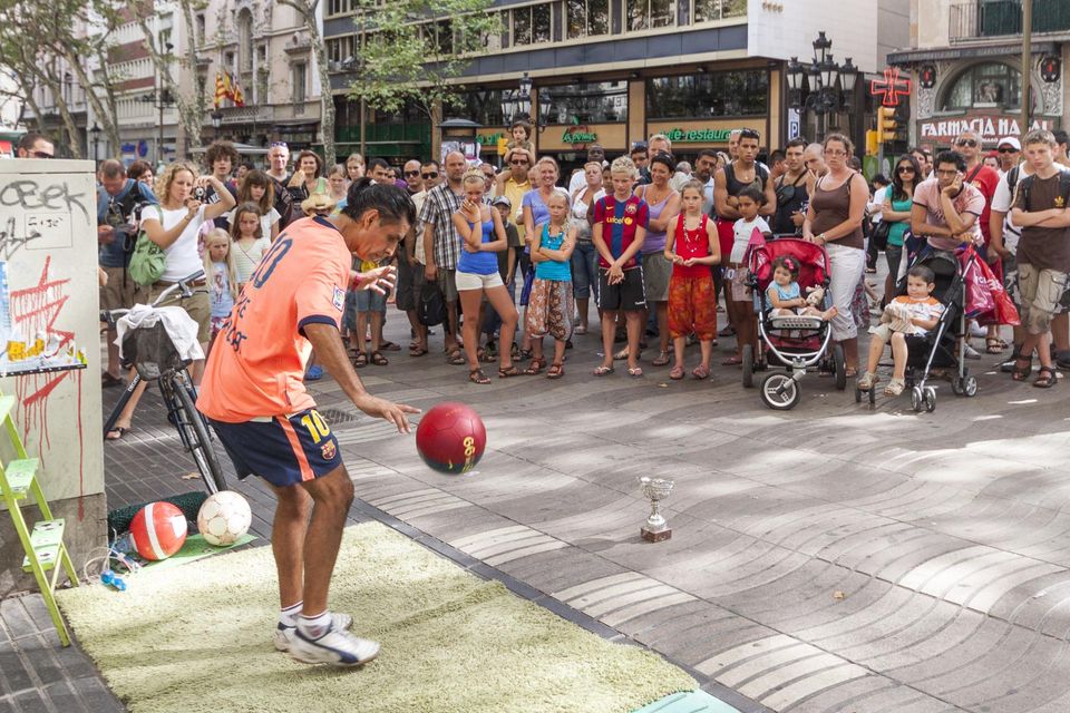 Street footballer juggling a red ball in front of a crowd