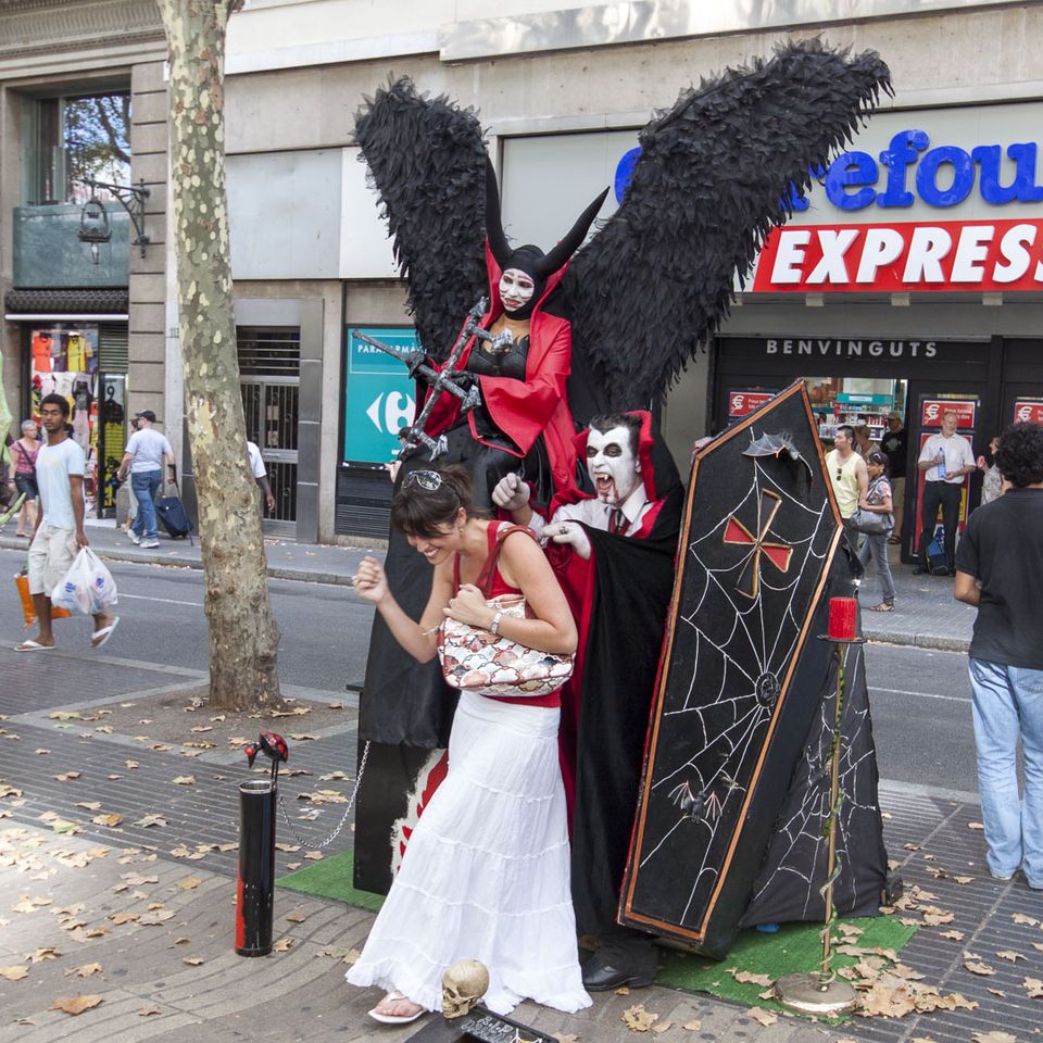 Performer in red vampire costume with black wings beside a coffin