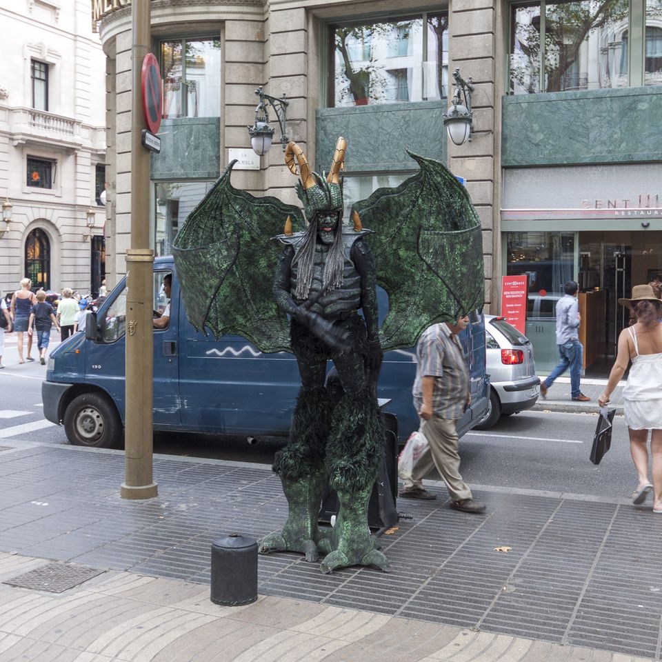 Winged green gargoyle-style living statue beside a van