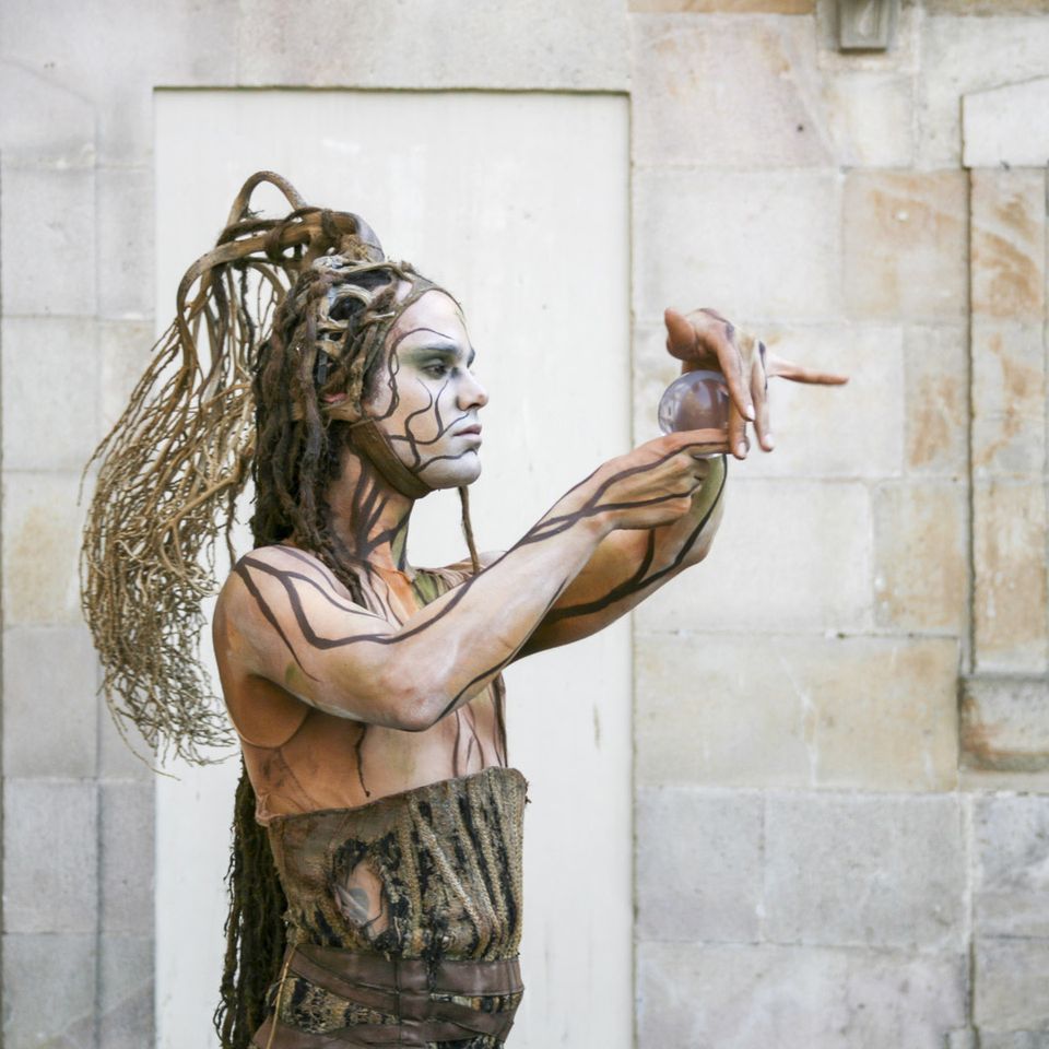 Painted performer with long dreadlocks reaching out a hand