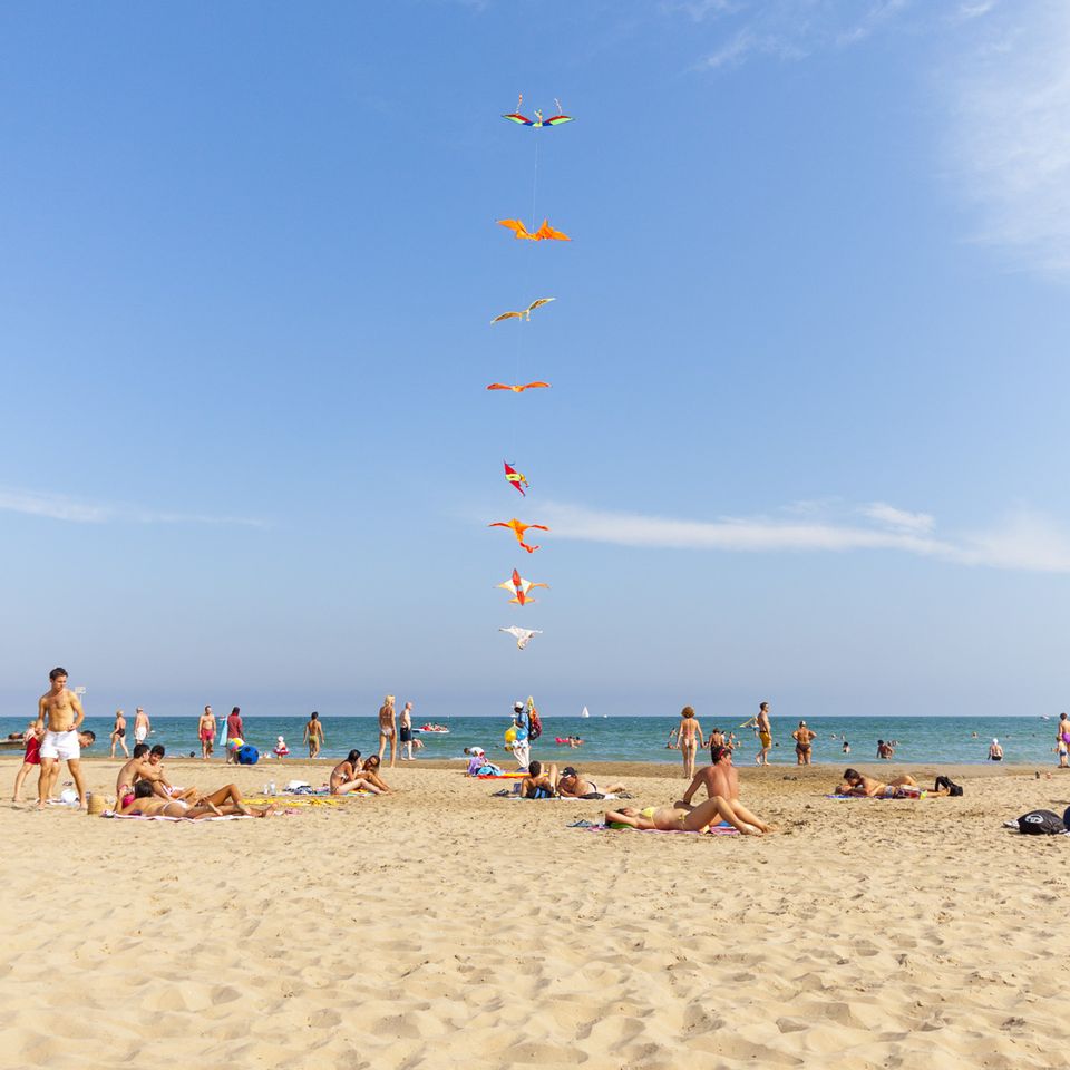 Chain of colourful kites rising above sunbathers on the beach