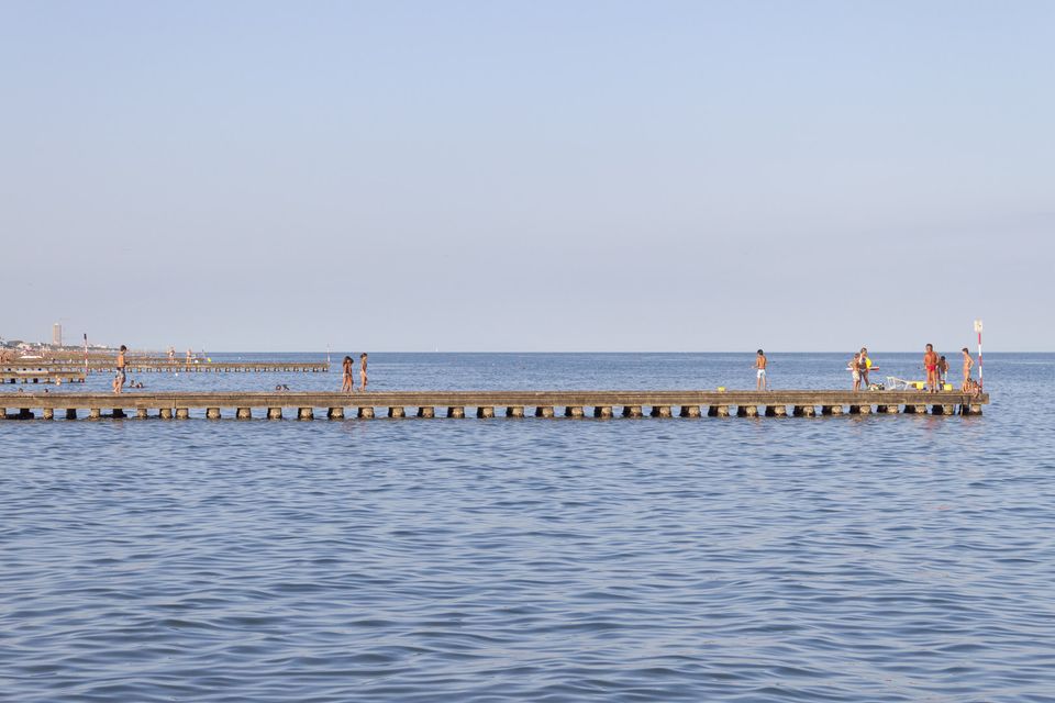 Wooden breakwater stretching into calm water with people walking on it