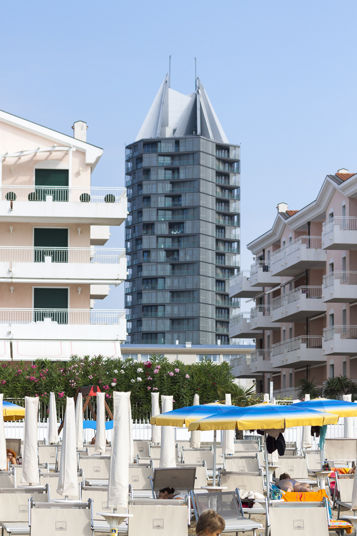 Tall dark glass tower rising behind sunshades and beach hotels
