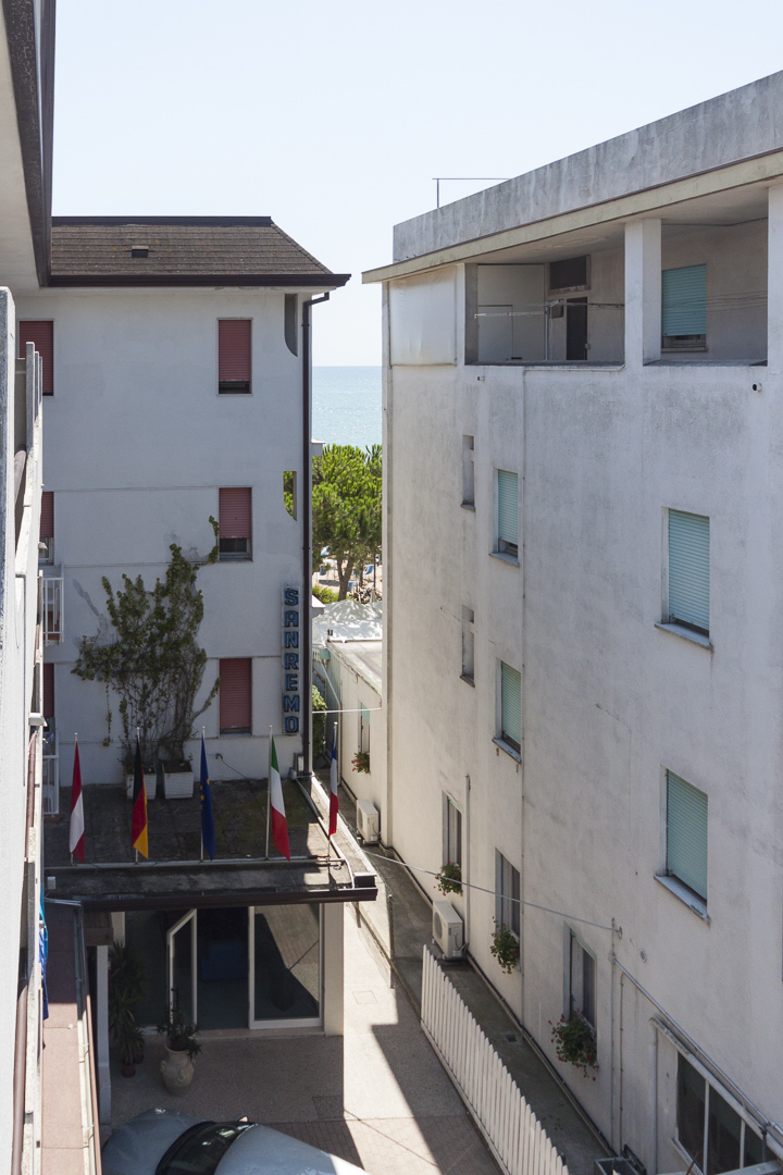 Narrow gap between white hotels with flags and a glimpse of sea