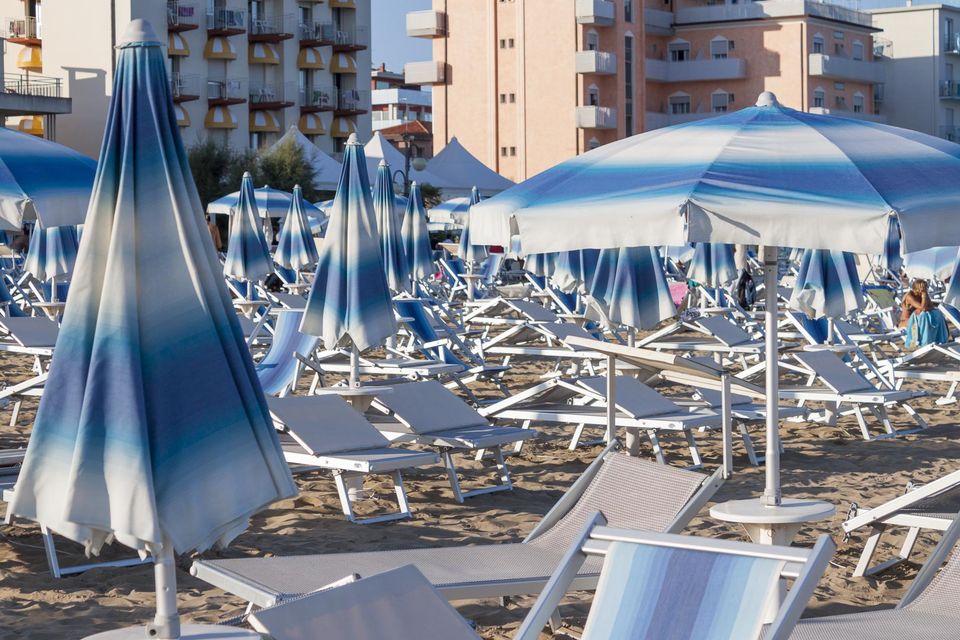 Blue-striped umbrellas and empty sunloungers in front of hotels