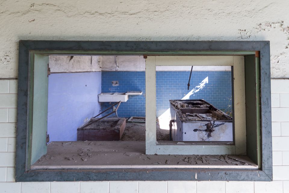 Window opening onto a derelict kitchen with blue tiles
