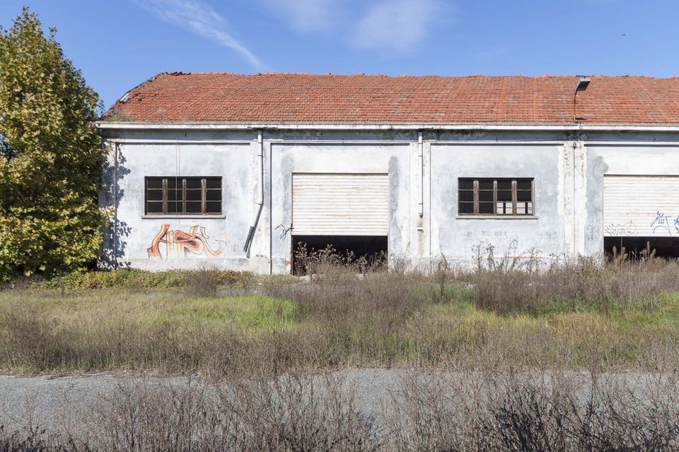Warehouse with a red tiled roof, roller doors and graffiti beyond dry grass