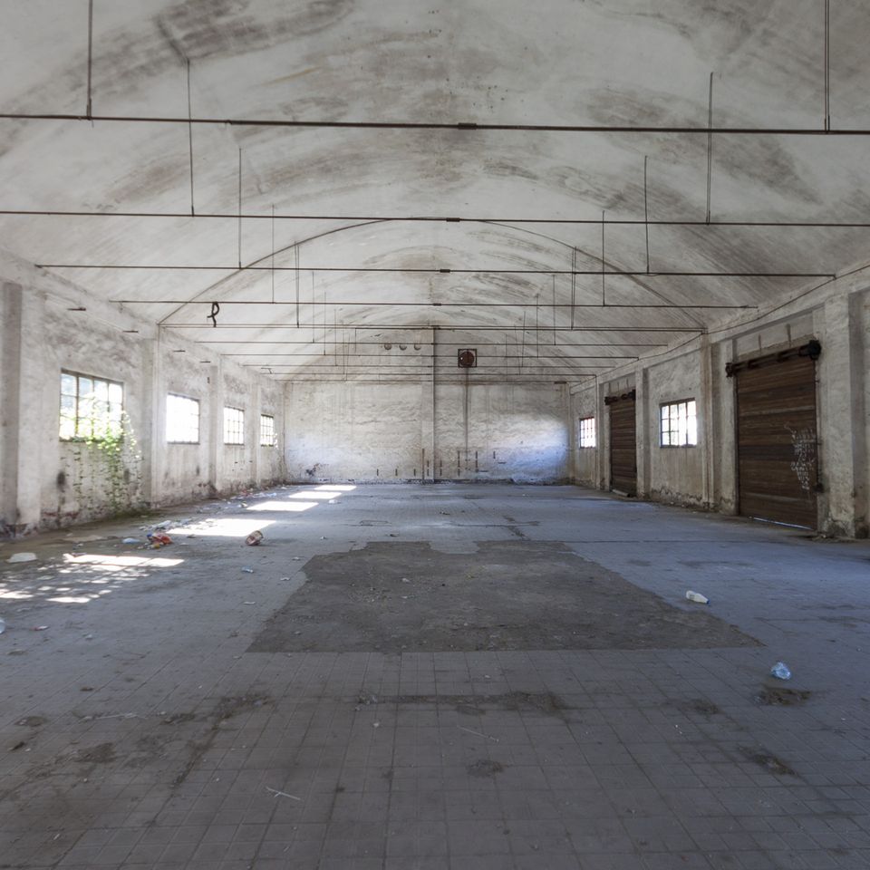 Vaulted empty hangar with roller doors and a dirty tiled floor