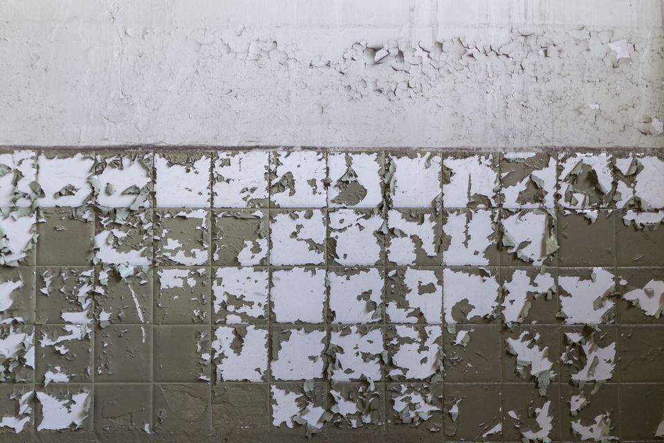 White tiles peeling from a grey wall