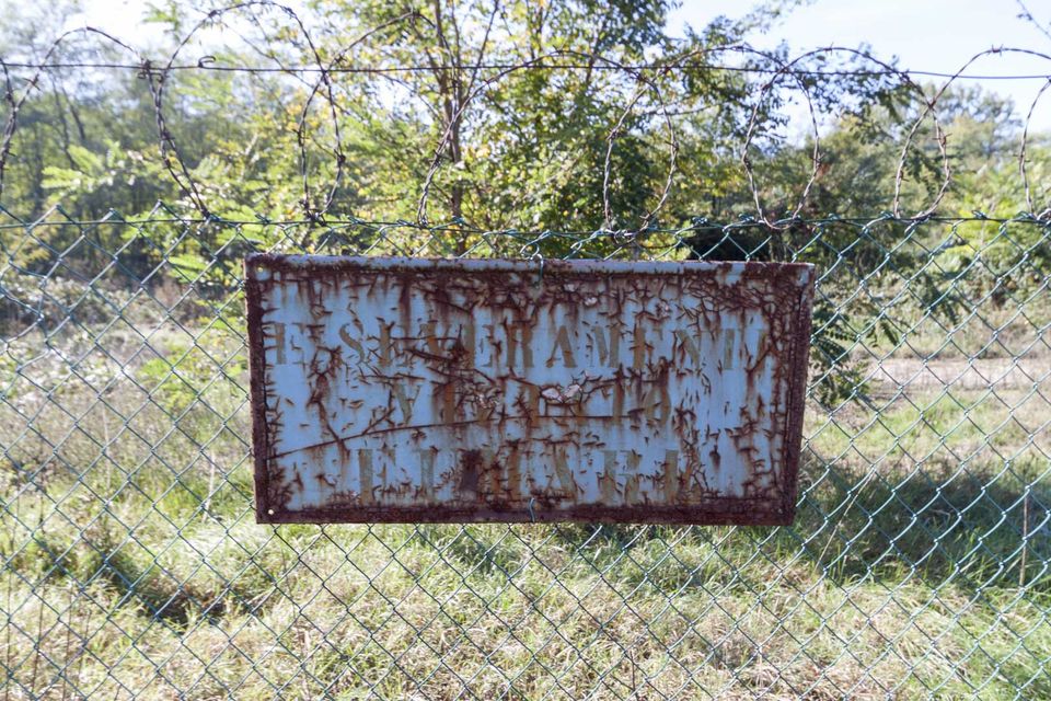 Rusted sign on a chain-link fence topped with barbed wire