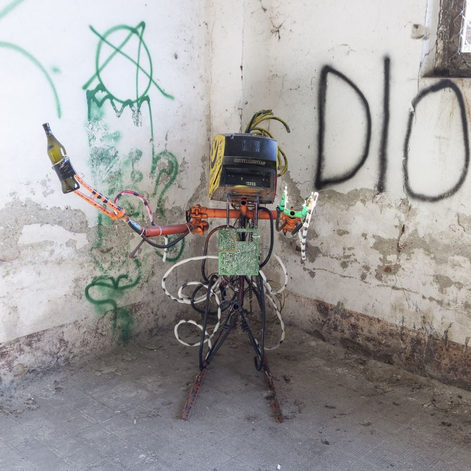 Small scrap-metal robot sculpture in a graffiti-covered corner