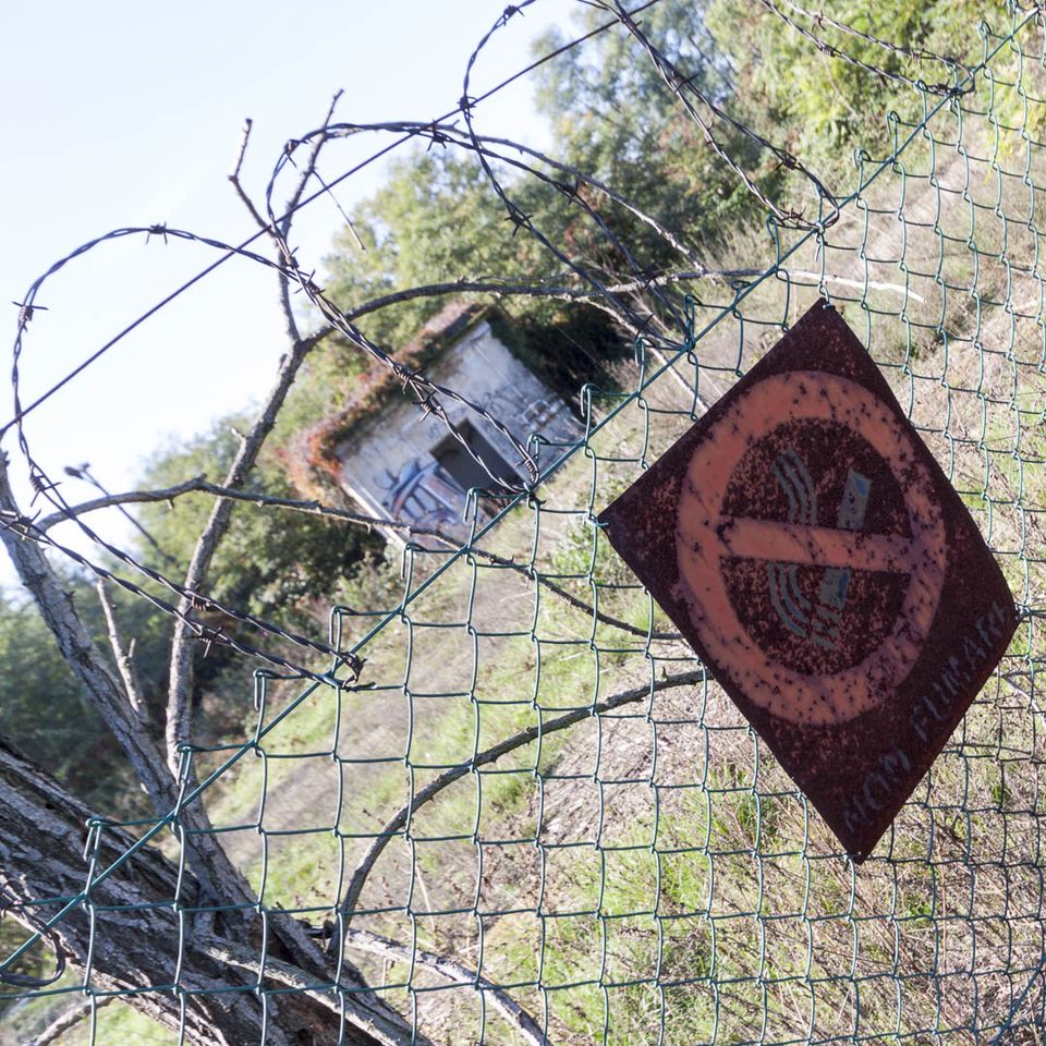 Rusted no-smoking sign on a barbed-wire fence with a small hut behind