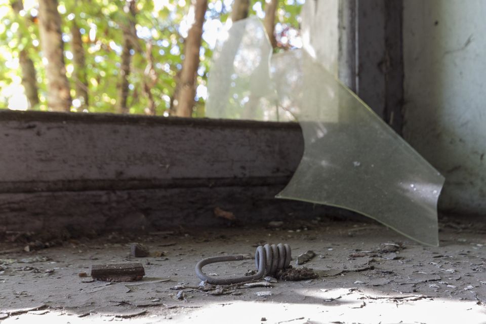 Shard of glass and a coiled spring on a windowsill with trees outside