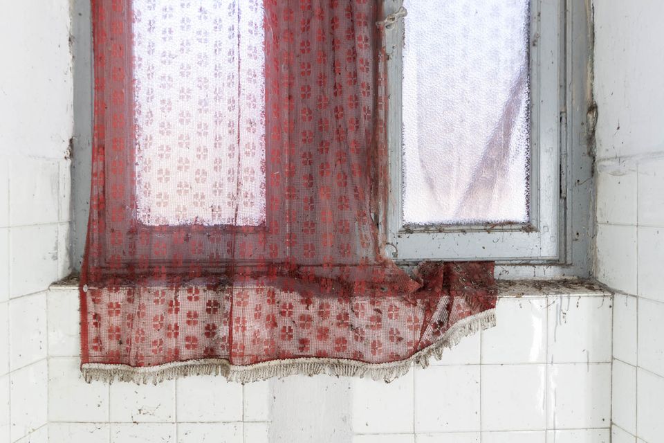 Torn red lace curtain over a window in a white-tiled room