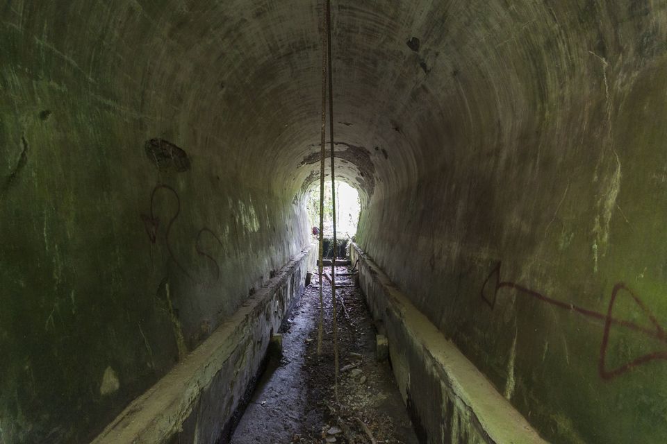 Moss-green concrete tunnel with a channel and light at the far end