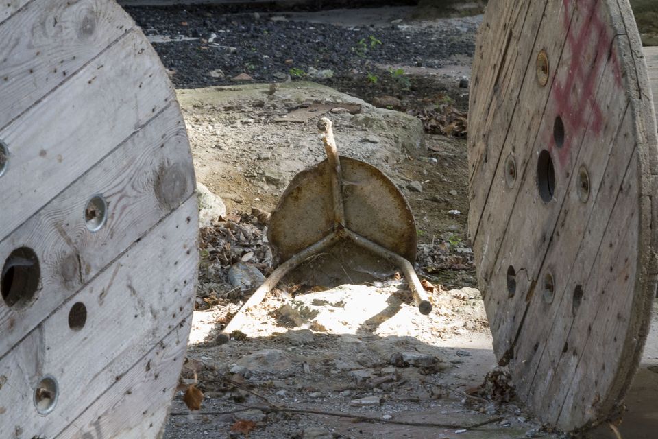 Upturned metal stool between two wooden cable reels