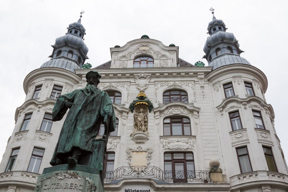 Bronze printer statue before an ornate cream facade with twin domes