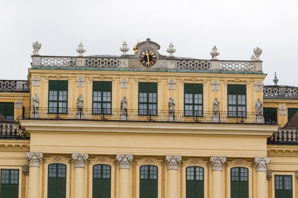 Yellow palace facade with a clock, balustrade and statues