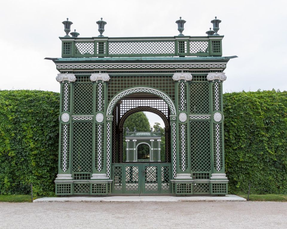 Green lattice garden pavilion in front of a tall hedge
