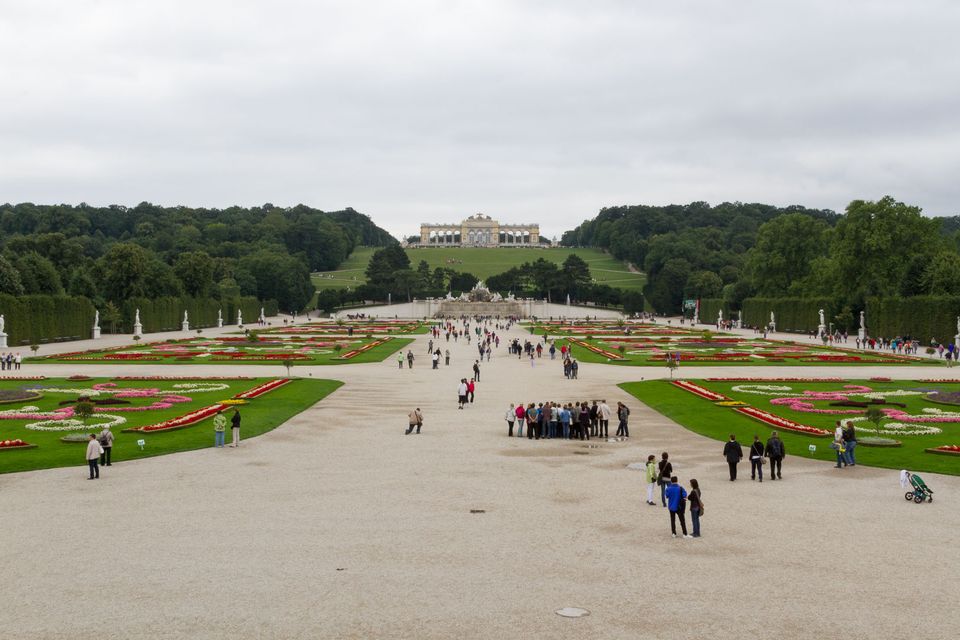 Formal flower-bed gardens leading up to a hilltop colonnade with visitors