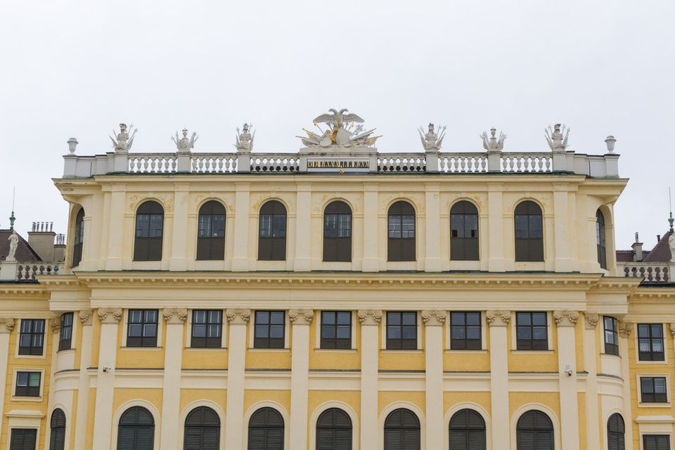 Symmetrical yellow palace facade with arched windows and rooftop statues