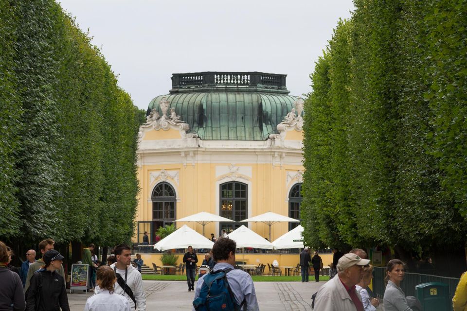 Domed yellow pavilion beyond a hedge avenue and café umbrellas