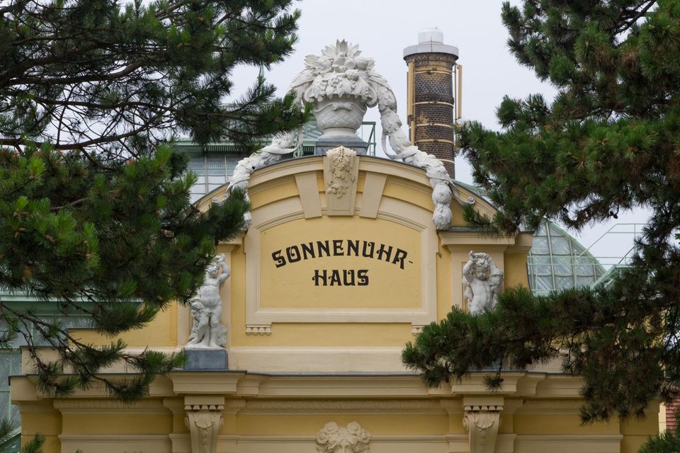 Yellow pavilion marked Sonnenuhrhaus with a sculpted urn among pines