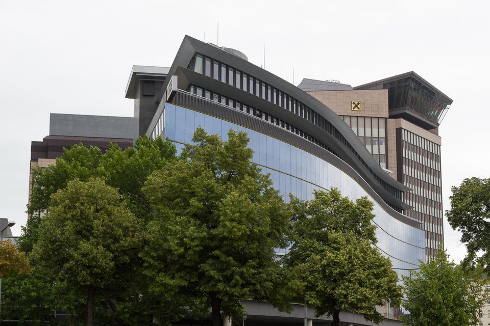 Curving glass office building behind green trees