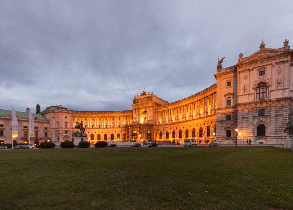 Curved palace wing glowing orange at dusk above a dark lawn