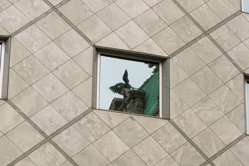 Stone-clad facade window reflecting an eagle statue and green roof