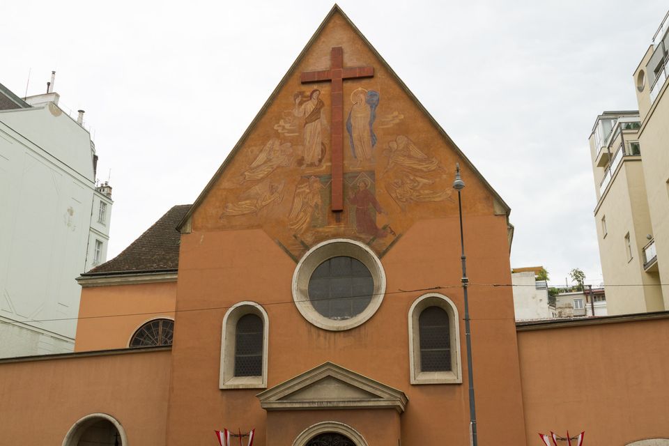 Orange chapel facade with a faded fresco and a large cross