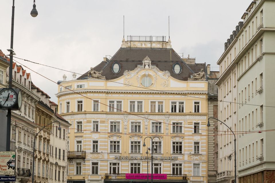 Cream-coloured hotel facade with a dark mansard roof and a street clock
