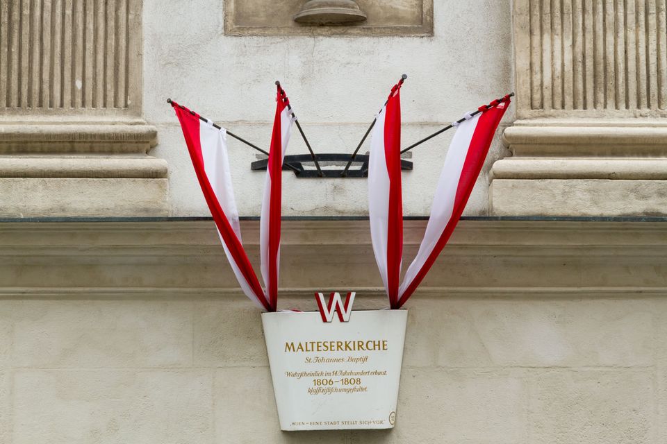 Red-and-white flags above the nameplate of a Maltese church