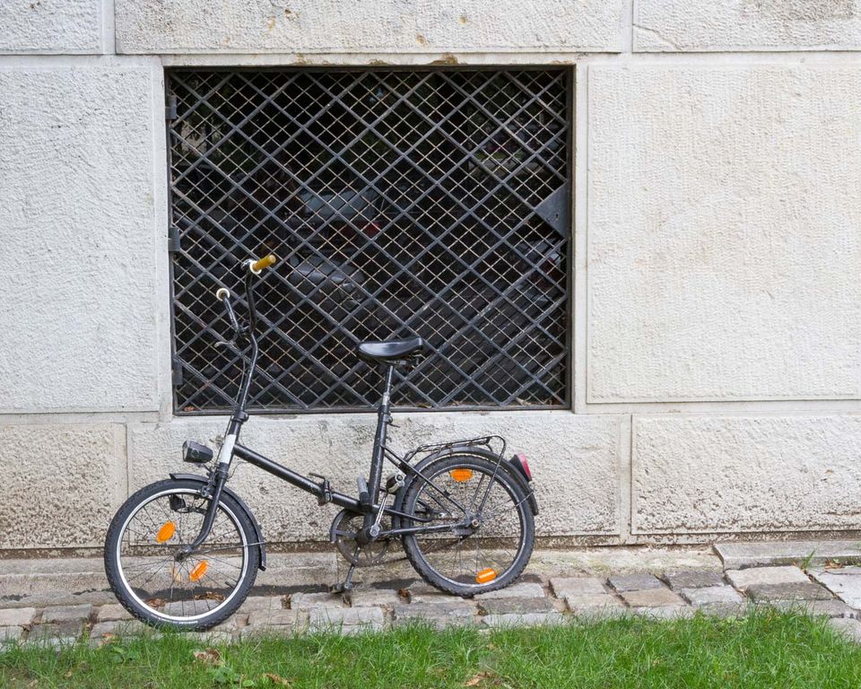 Folding bicycle leaning against a stone wall with a barred window