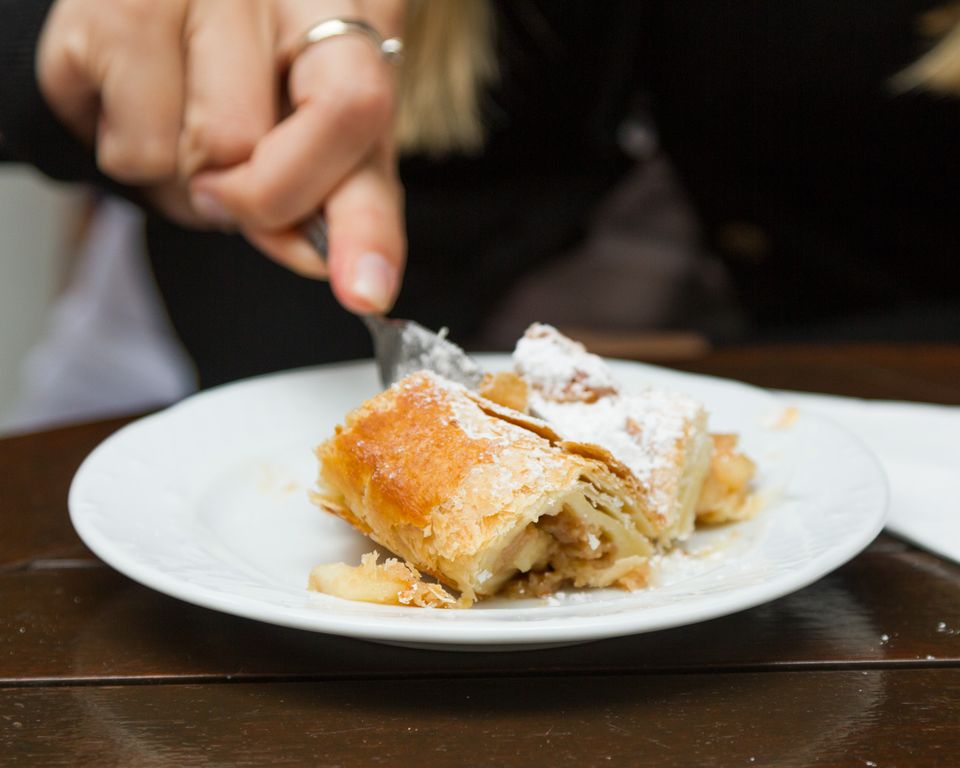 Fork cutting into apple strudel dusted with sugar on a white plate