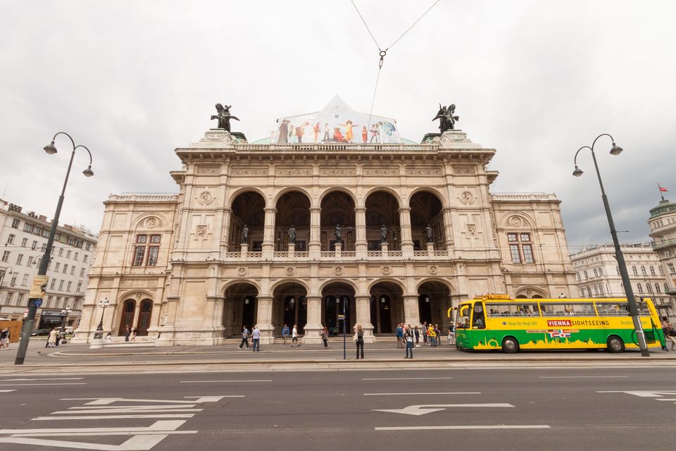 Opera house facade with arched loggia and a yellow sightseeing bus
