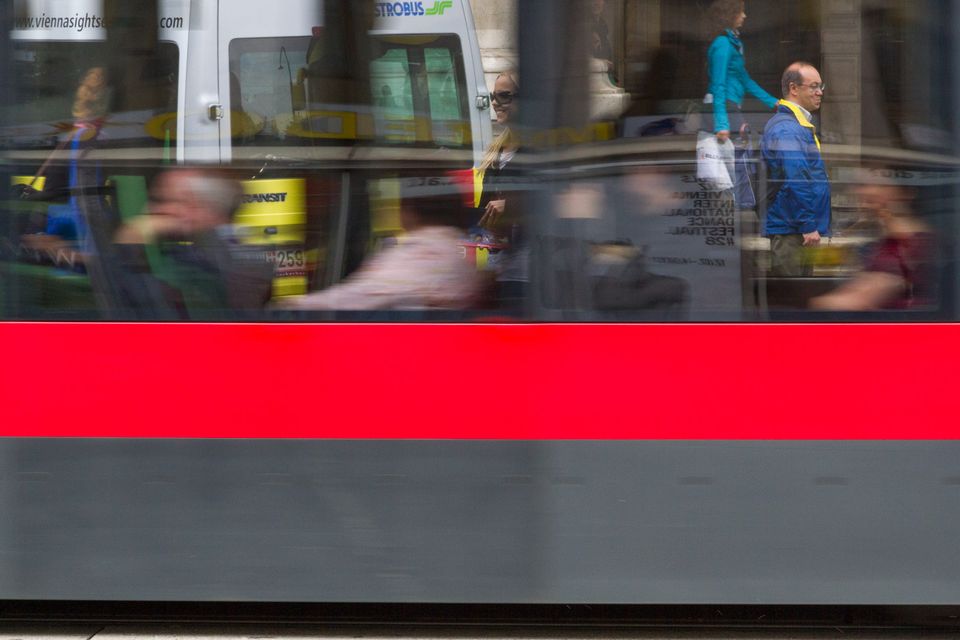 Motion-blurred tram with a red stripe reflecting passers-by