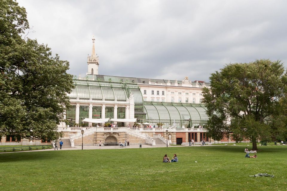 Glass-roofed palm house beyond a lawn with people sitting