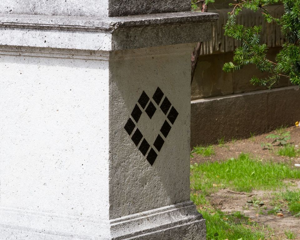 Corner of a stone pillar with a black diamond ornament beside grass