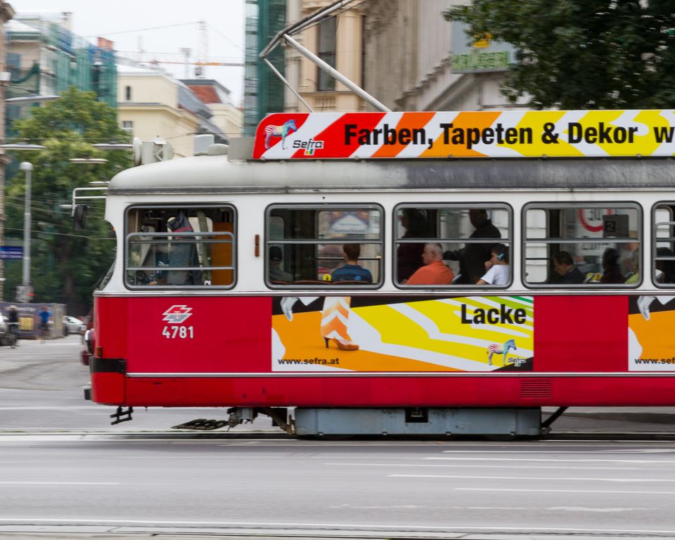 Red-and-white tram with colourful advertising speeding along the street