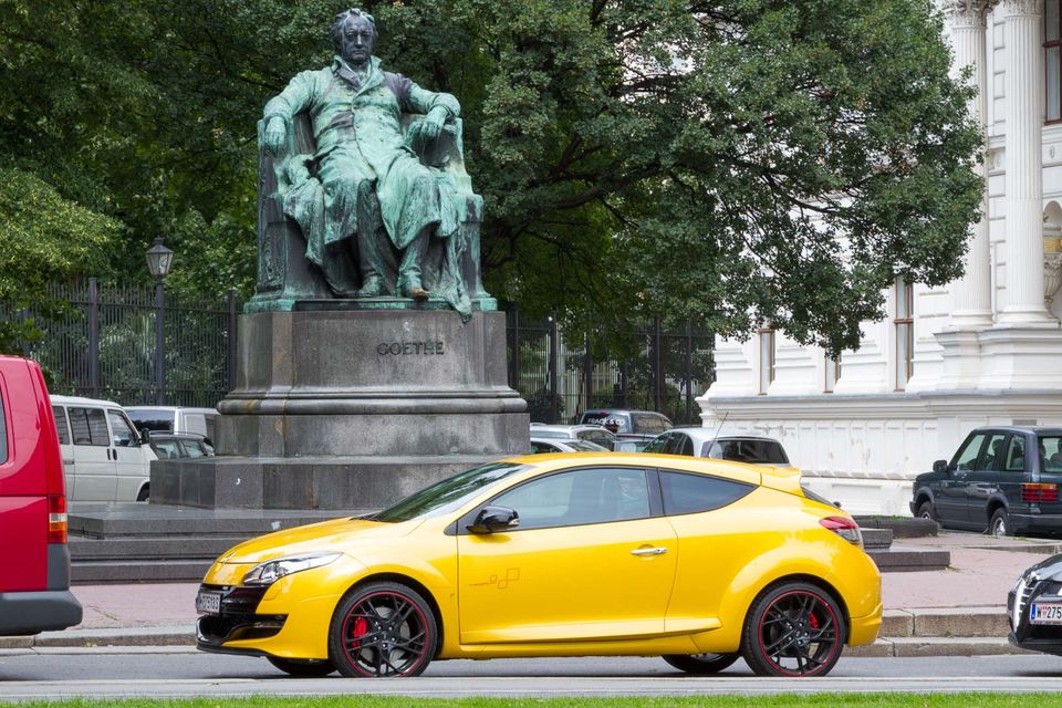 Seated green bronze statue behind a yellow sports car