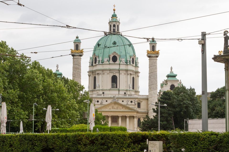 Green-domed baroque church between two tall columns behind a hedge