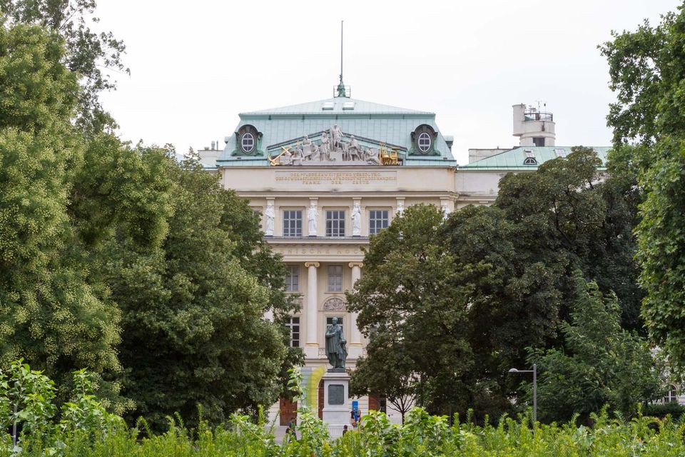 Neoclassical building with a green roof and a statue seen through trees