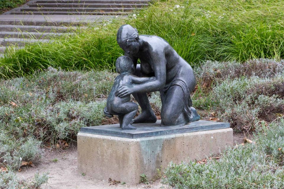 Bronze mother kneeling with a child in a planted garden