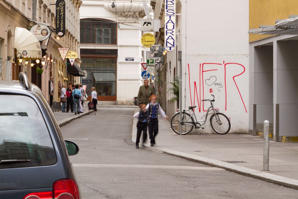Two children crossing a quiet street past a bicycle and red graffiti
