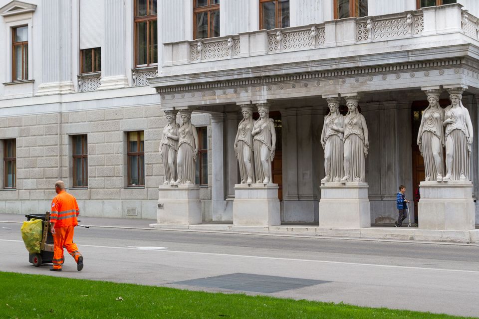 Stone caryatids under a portico with a street sweeper in orange