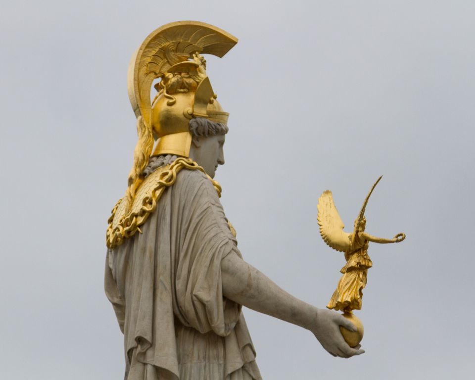 Statue with gilded helmet holding a small winged figure against grey sky