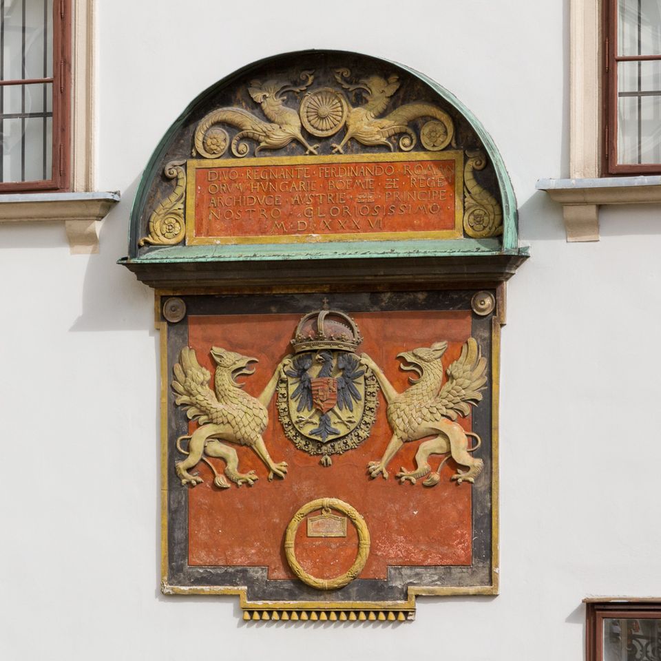 Painted heraldic plaque with griffins and a crown on a white wall